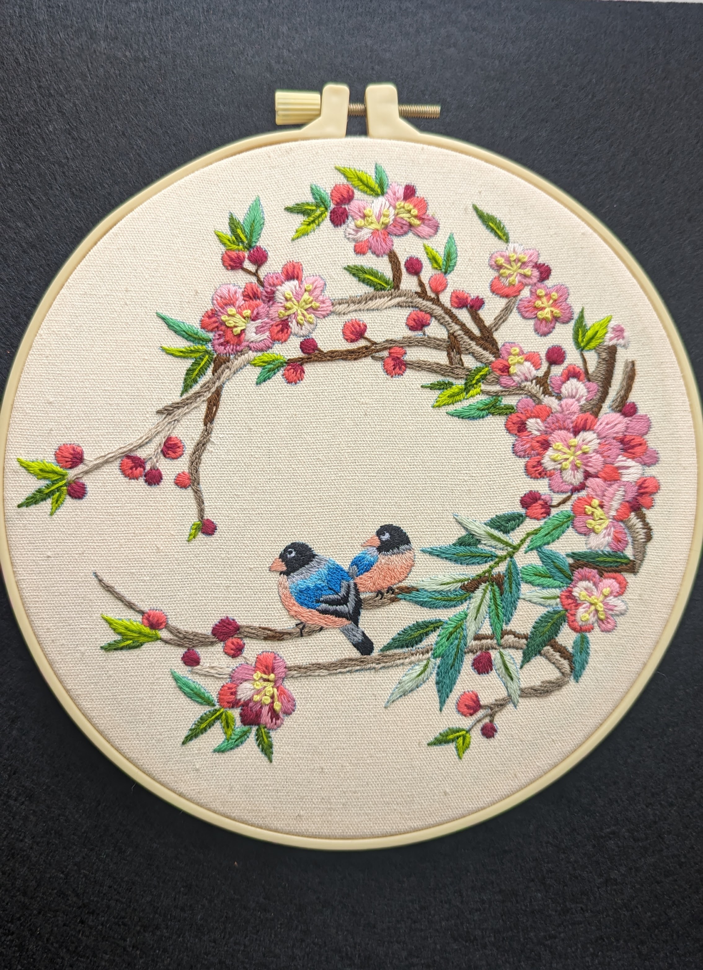 Hand embroidery of two finches on a flowering branch, worked in a wreath.